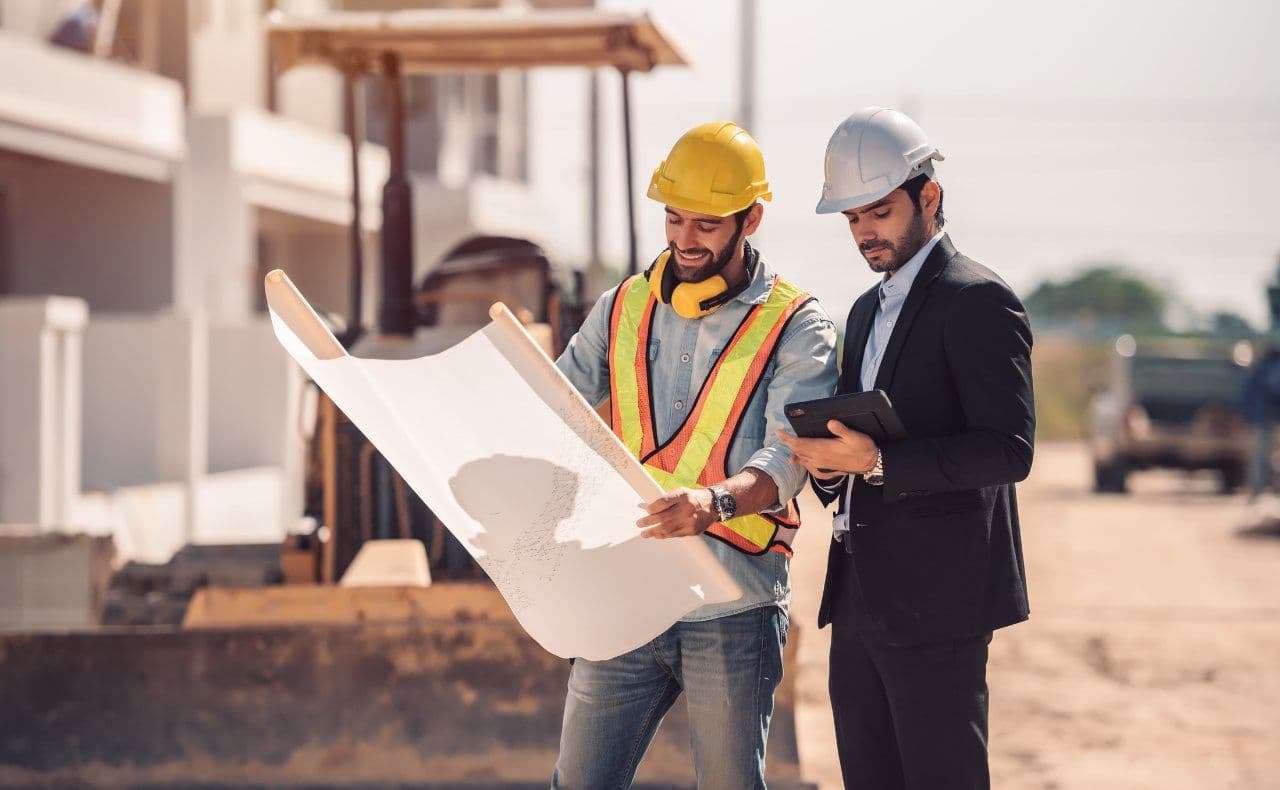 Engenheiro e trabalhador analisando planta no canteiro