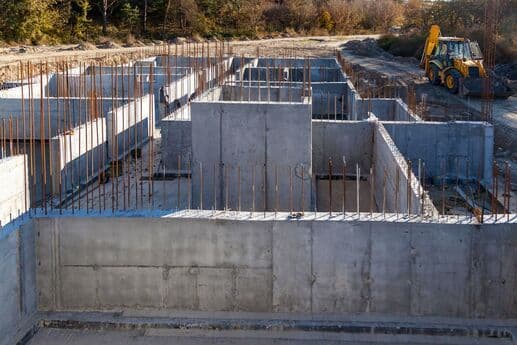 Obra em construção com fundações de concreto e ferros expostos.